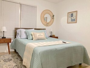Un dormitorio con una cama, dos mesitas de noche, un tocador, un espejo y un cuadro en la pared.