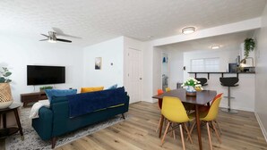 Ein modernes Wohnzimmer mit einem türkisfarbenen Sofa, gelben Sesseln und einem Flachbildfernseher.