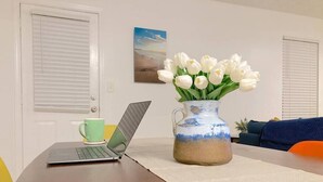 Ein Laptop auf einem Tisch mit einer Vase weißer Tulpen und einer grünen Tasse.