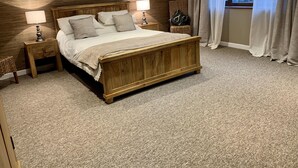 A bedroom with a wooden bed, two bedside tables with lamps, a decorative wall piece, and a window with curtains. - The Stables, Lovely Country Apartment in a Converted Barn (Wells)