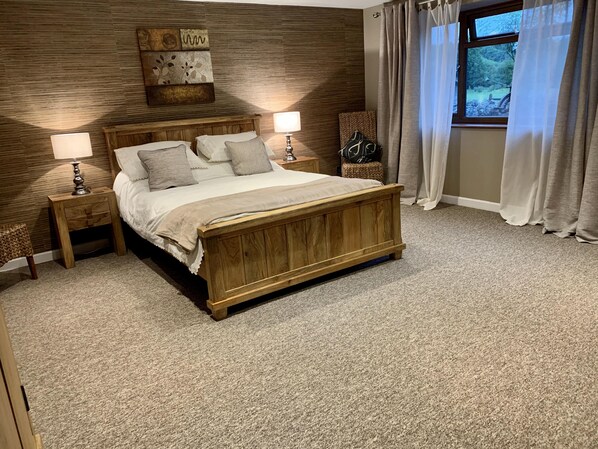 A bedroom with a wooden bed, two bedside tables with lamps, a decorative wall piece, and a window with curtains.