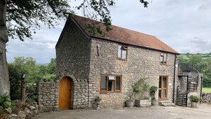 A stone house with a red-tiled roof, a wooden door, and a small staircase leading to an upper level. - The Stables, Lovely Country Apartment in a Converted Barn (Wells)