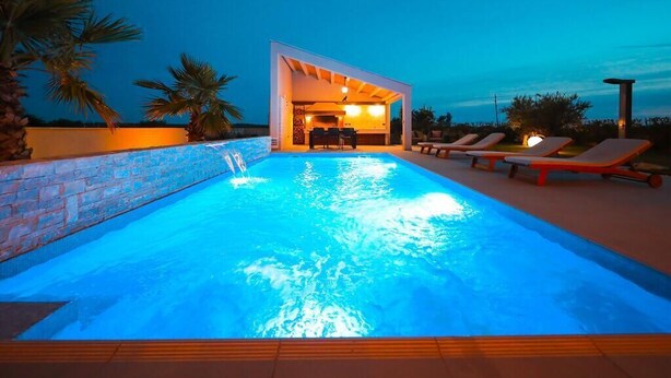 A swimming pool with a modern architectural structure in the background, surrounded by lounge chairs. - Villa Petra (Nin)