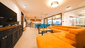 A modern living room with a large orange sofa, a flat-screen TV, and a dining area with blue chairs. - Villa Petra (Nin)