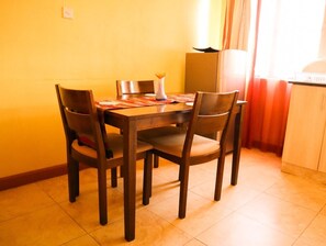 Un comedor con una mesa y sillas de madera, un jarrón sobre la mesa, y una cocina con armarios y un refrigerador.