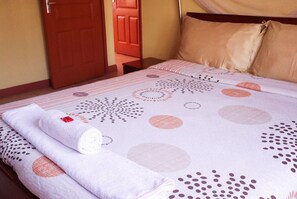 Una cama bien tendida con una colcha estampada, una toalla blanca enrollada y una almohada color beige.