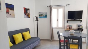 Un salon comprenant un canapé, une table à manger avec des chaises, un porte-manteau, un téléviseur et des œuvres d’art accrochées aux murs.
