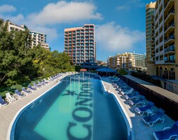 Una piscina con sillas de descanso y un edificio al fondo.