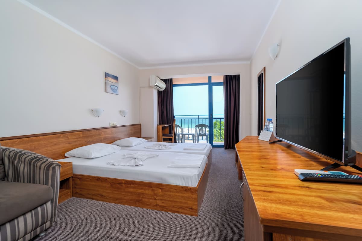 A hotel room with a bed, a desk with a TV, a sofa, and a balcony with a view.