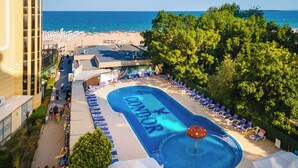 Un espace piscine aménagé dans un complexe hôtelier, comprenant une grande piscine, des chaises longues et une vue sur la plage et l’océan.