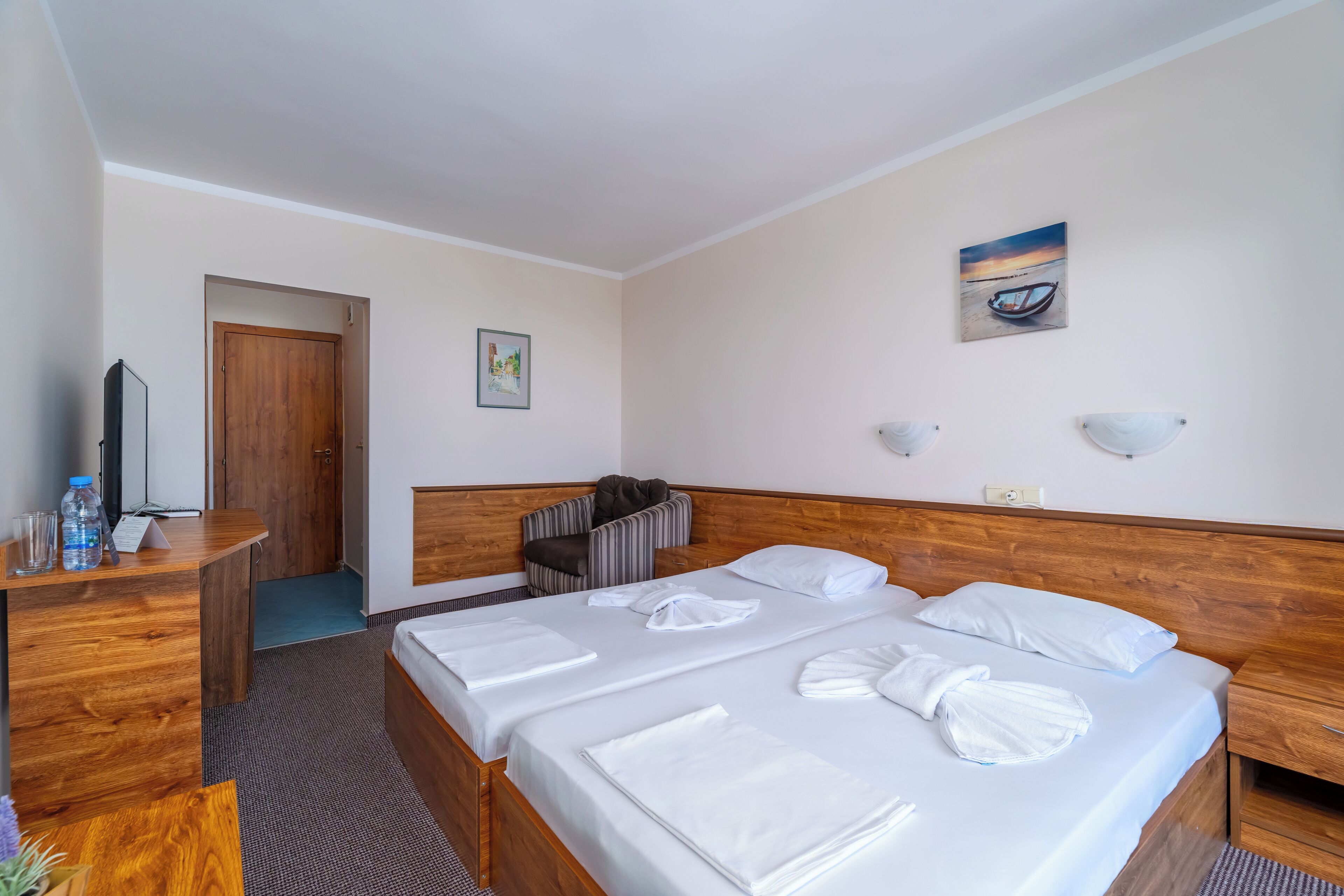 A hotel room with two beds, a wooden desk, a chair, a television, and a painting on the wall.