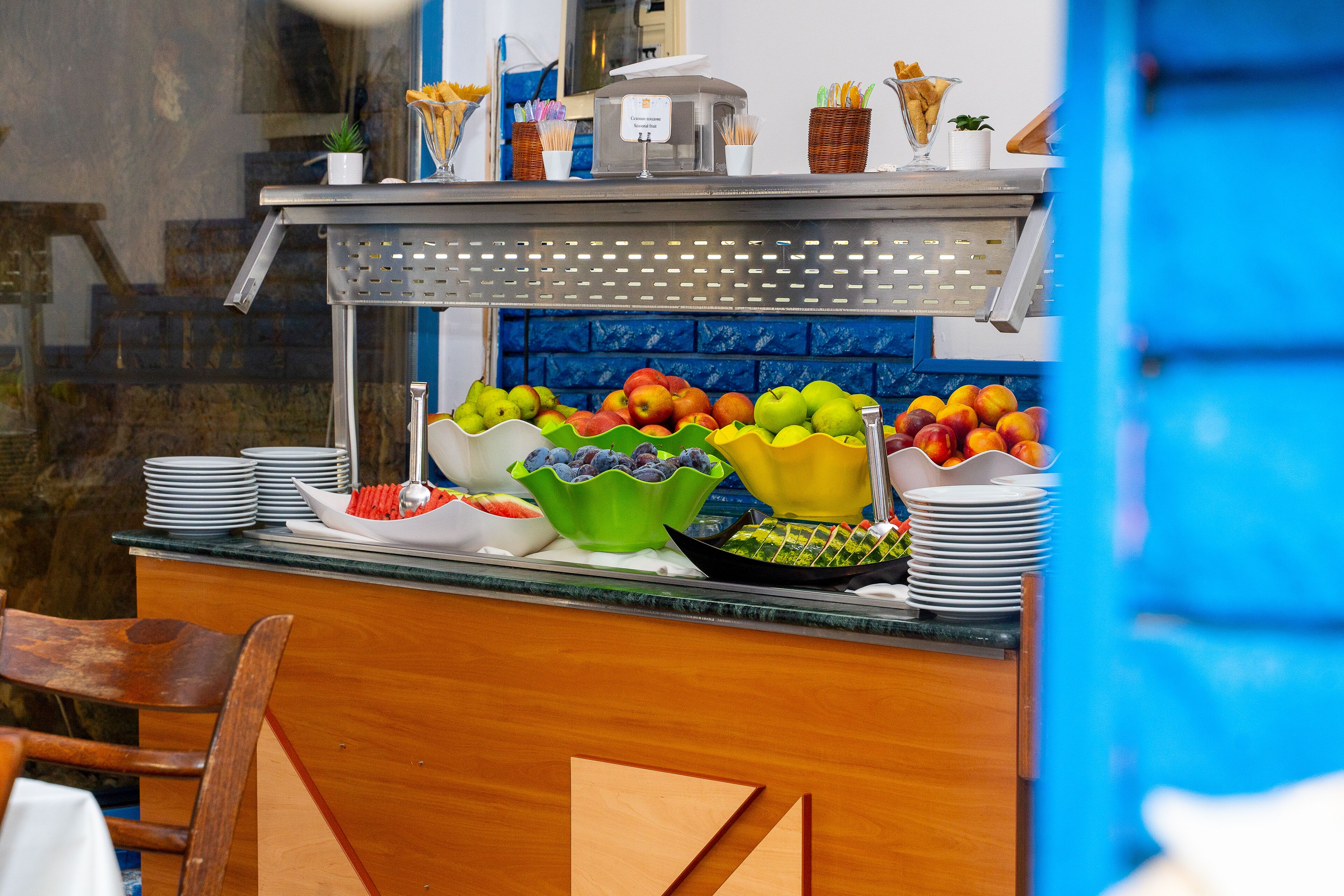 A buffet counter with various fruits and bowls of food, a coffee machine, and a sign indicating a cashless payment option.