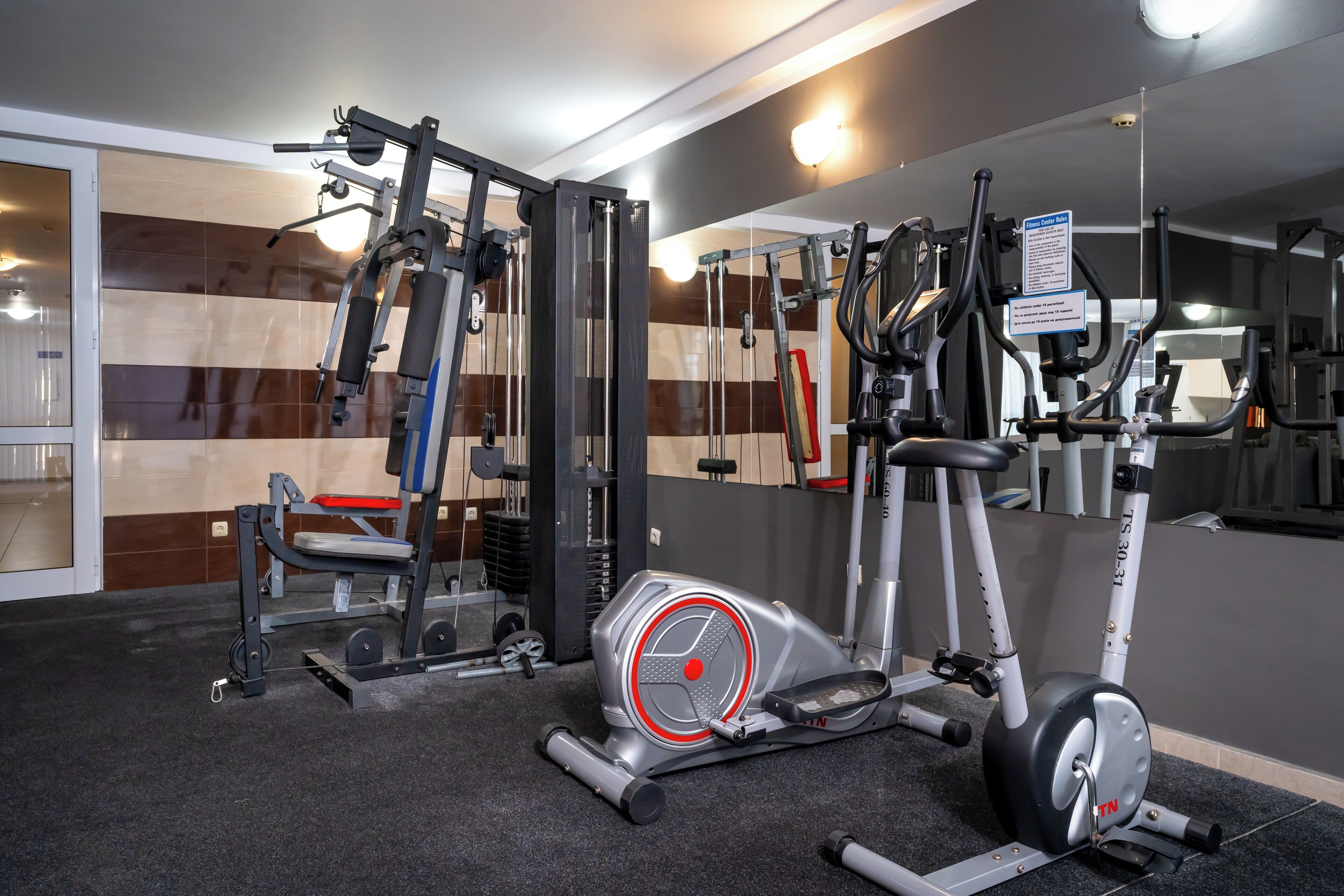 A gym with various exercise equipment, including a treadmill, weight machines, and a mirror wall.