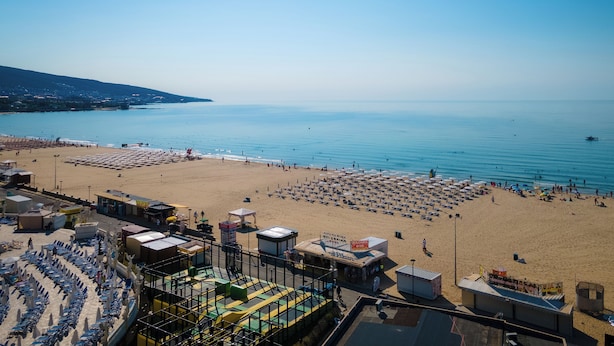 A beach with rows of sun loungers and umbrellas, a small building with signage, and a clear view of the sea. - MPM Hotel Condor - All Inclusive Light (Sunny Beach)