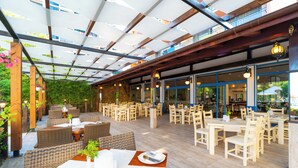 An outdoor dining area with wicker furniture, wooden tables, and a glass ceiling. - MPM Hotel Condor - All Inclusive Light (Sunny Beach)