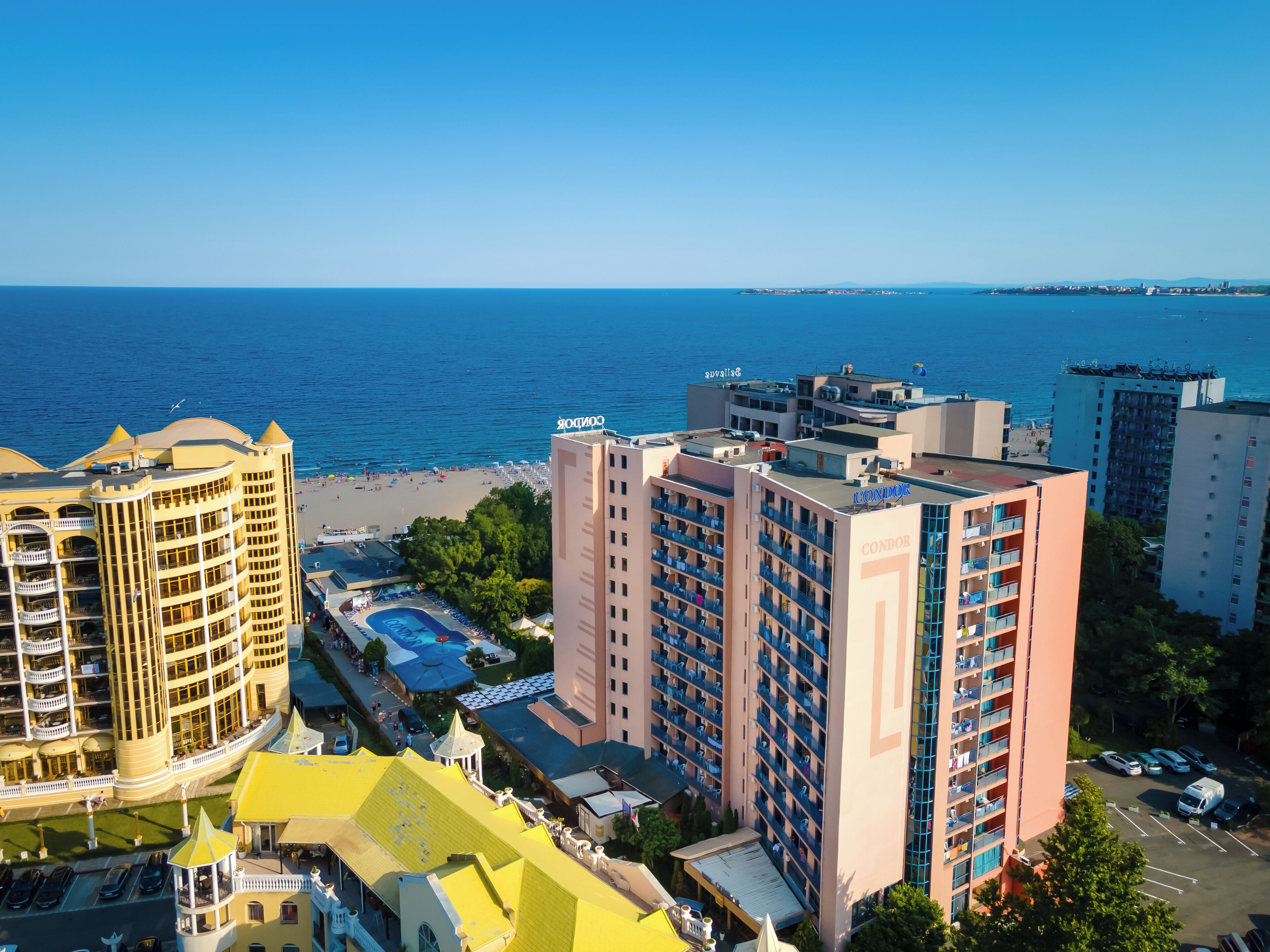 A high-rise hotel with multiple balconies, a swimming pool, and a beach view.