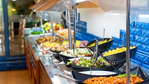 A buffet with various food options, including salads, pasta, and other dishes, arranged on a counter with a blue tiled wall in the background. - MPM Hotel Condor - All Inclusive Light (Sunny Beach)