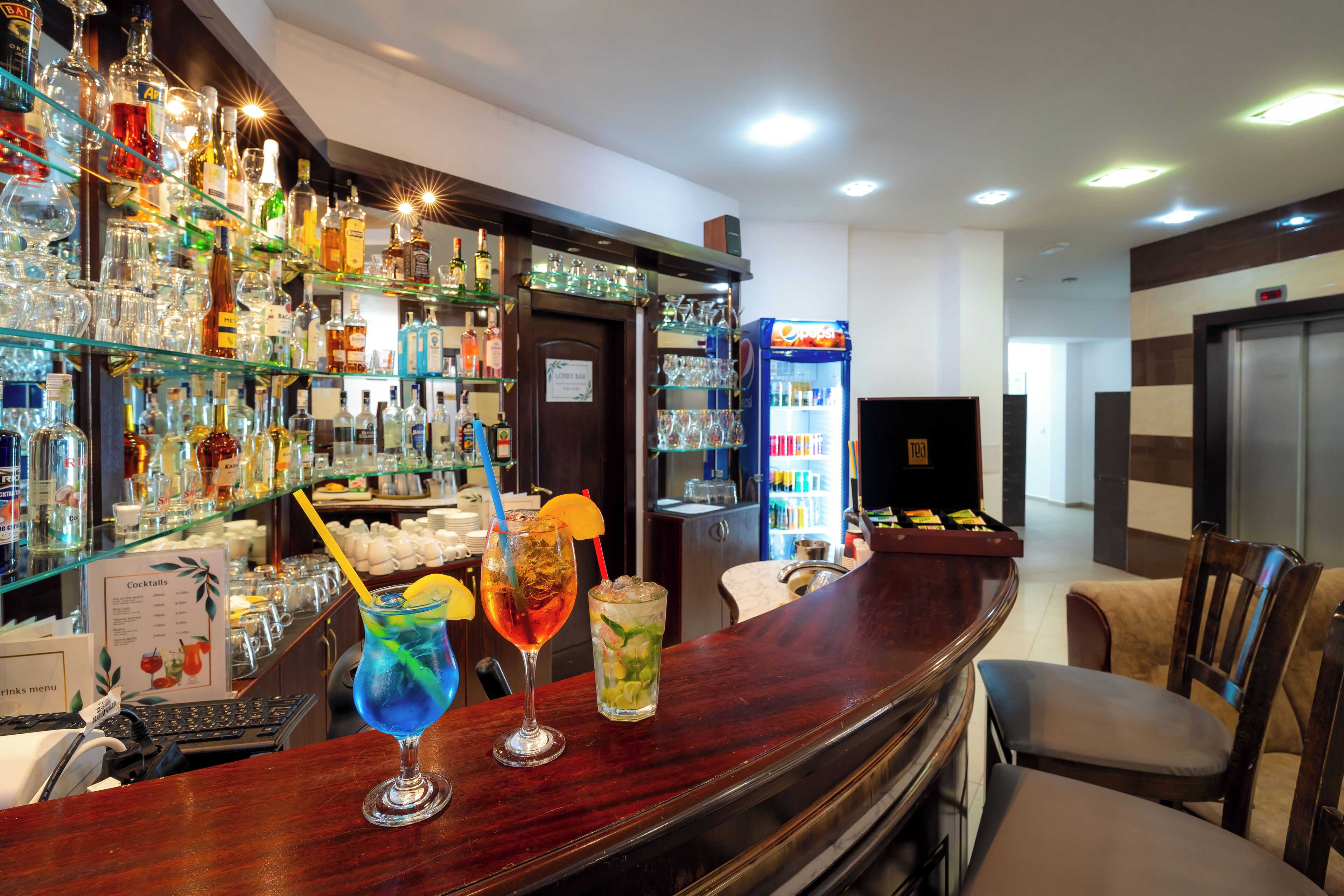 A bar area with a variety of liquor bottles, two cocktails on the bar counter, and a Pepsi vending machine.