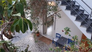 Un petit espace extérieur clos, doté d’un sol en béton, d’une plante en pot, d’une chaise bleue et d’une table.