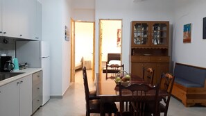 A compact kitchen with white cabinets, a coffee maker, and a dining area with a wooden table and chairs.