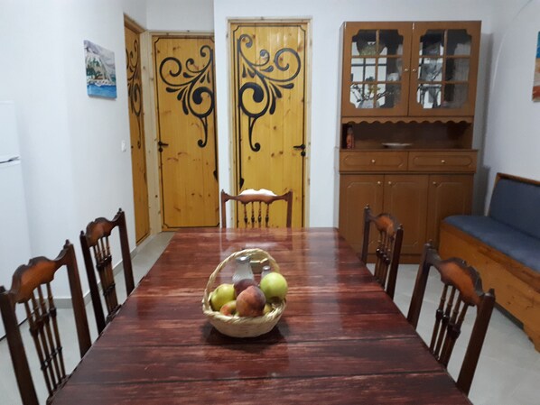 A dining area with a wooden table, chairs, a fruit basket, and wooden doors with decorative designs.