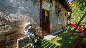 A rustic building with a weathered exterior, a wooden door with a flower decoration, and a small garden area with artificial grass and a wooden play structure. - Atrium Penzion (Poprad)