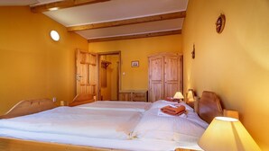 A double bed with wooden headboards, a bedside table with a lamp, and wooden wardrobes in a room with yellow walls and wooden beams. - Atrium Penzion (Poprad)