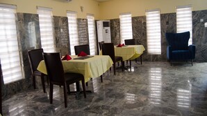 A dining area with marble flooring, tables with yellow tablecloths, and chairs. - En Apartment (Abuja)