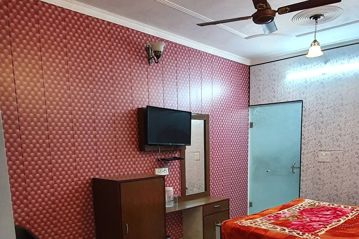 Une chambre à coucher comprenant un lit, un téléviseur, une armoire, un ventilateur de plafond et un mur rouge à texture.