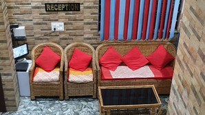 A reception area with a reception desk, wicker chairs with red cushions, a sofa with red cushions, and a striped curtain. - Delhi Homes By Lujo Hotels (Narendranagar)