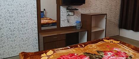 A hotel room with a bed, a television, a ceiling fan, and a wall-mounted light fixture.
