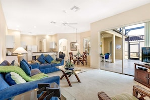 A spacious living room with a blue sofa, a glass coffee table, and a dining area with a table and chairs. - 527 - Beautiful Mediterranean Style Villa Close to Disney with Private Pool and Spa (Davenport)