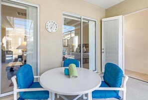 Un balcone con un tavolo rotondo e sedie blu, una porta scorrevole in vetro e una sveglia a parete.