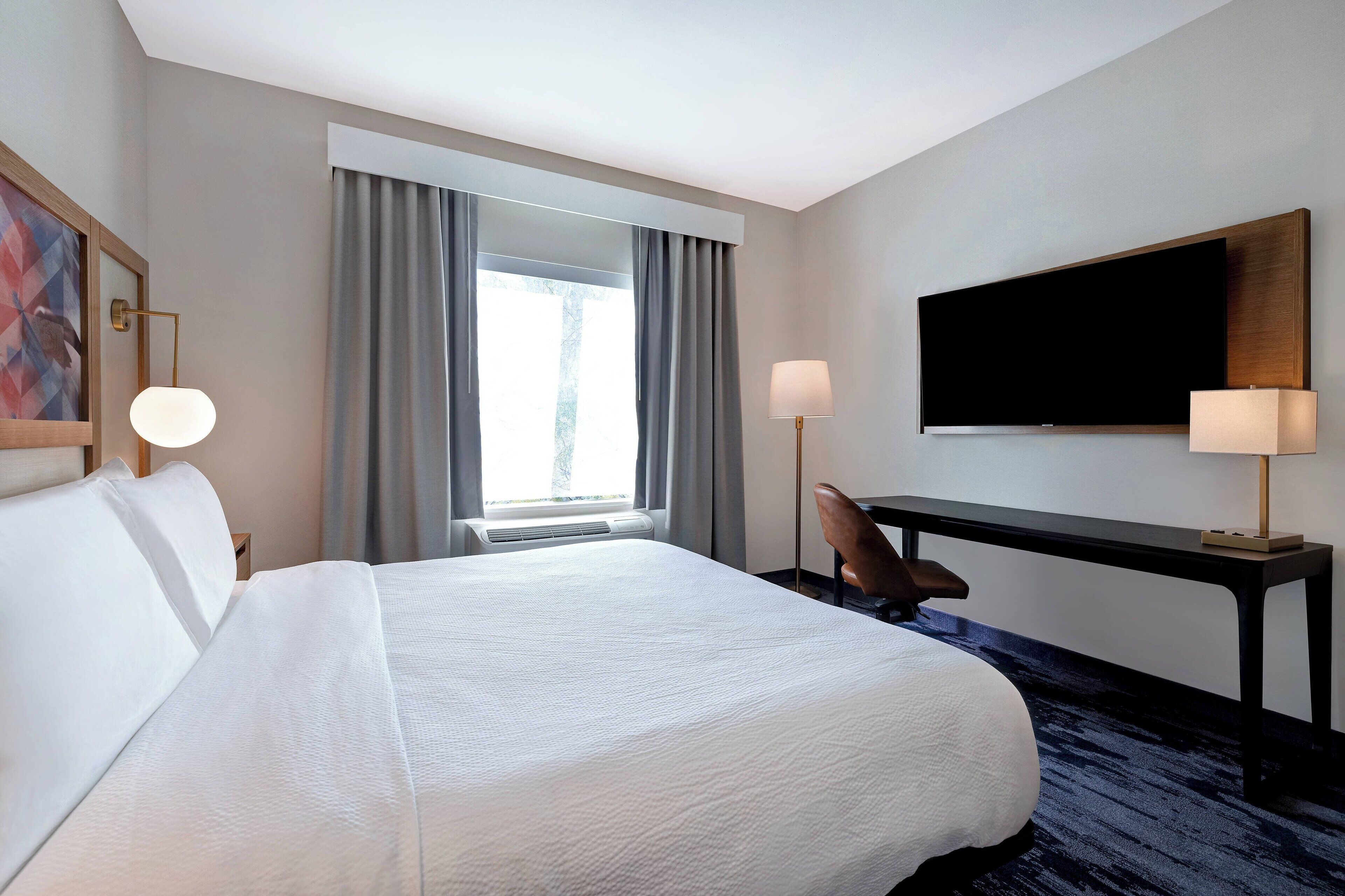 Hotelkamer met een groot bed, een bureau met een flatscreen televisie, een stoel en een raam met gordijnen.