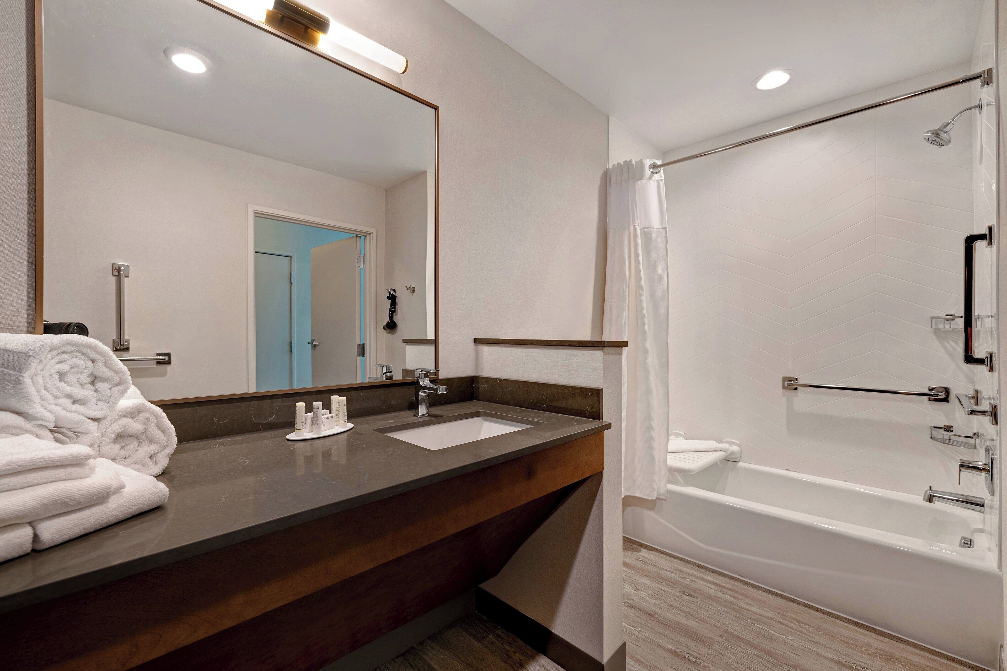 A modern bathroom with a dark wood vanity, a large mirror, a white sink, and a separate shower area.