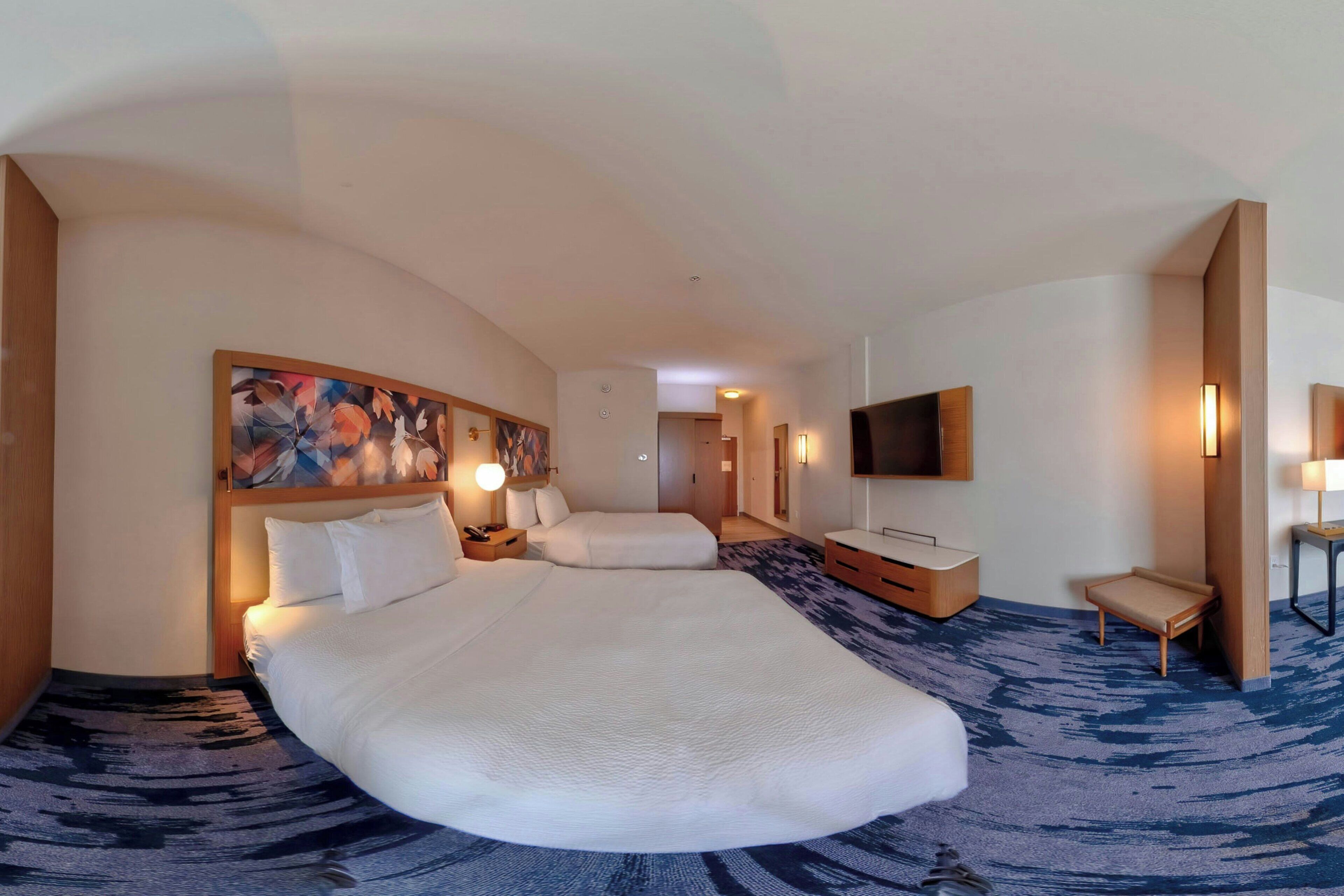 A hotel room with a large bed, a TV mounted on the wall, and a small seating area.