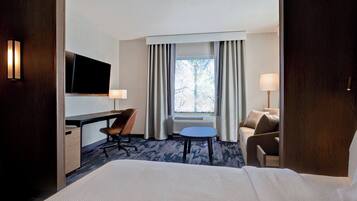 Habitación de hotel con cama, escritorio, silla, televisor y ventana con cortinas.