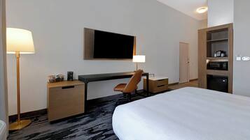 Habitación de hotel con una cama grande, un escritorio con silla, un televisor de pantalla plana montado en la pared, un microondas y una cafetera.