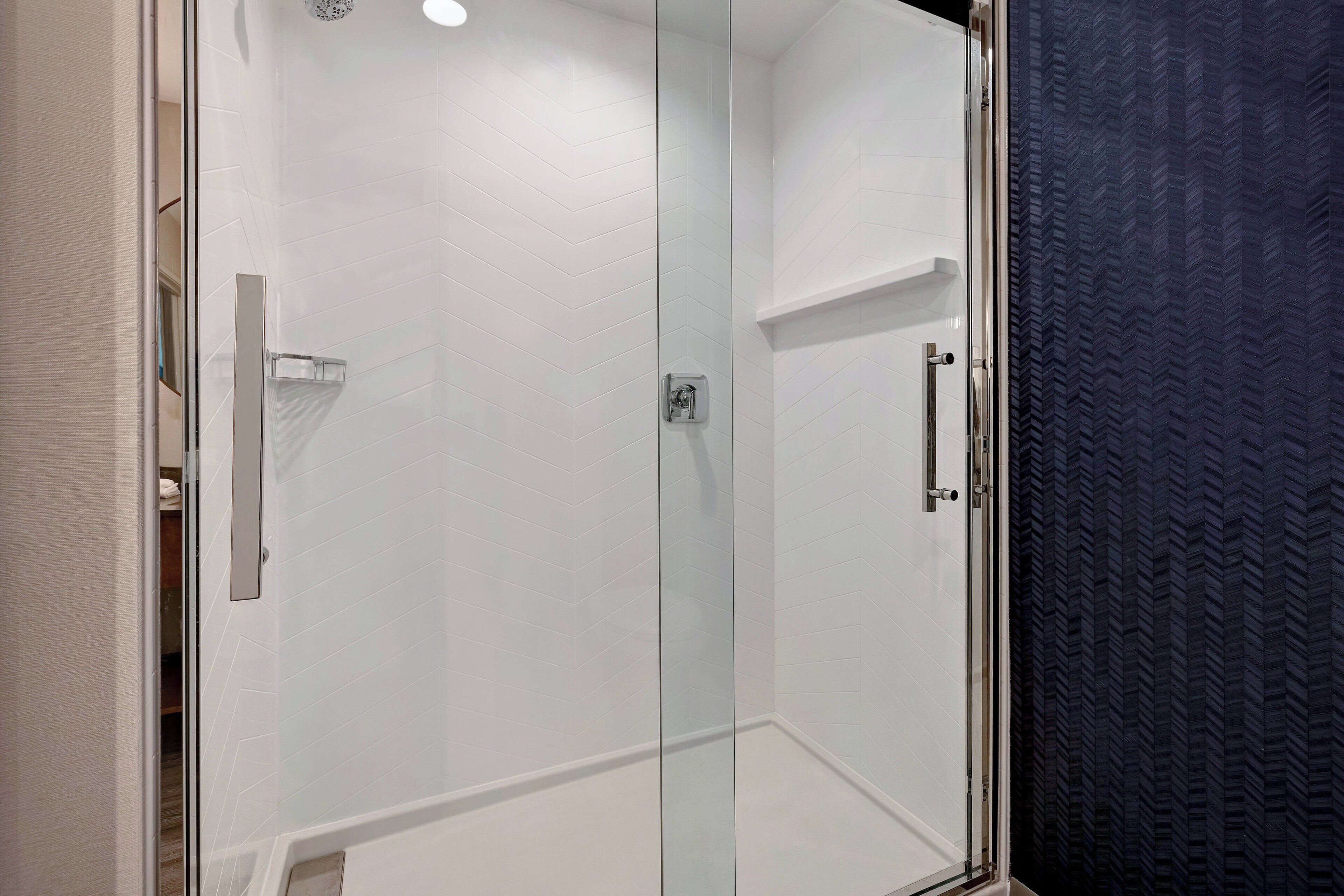 A glass-enclosed shower area with white tiled walls and a dark textured curtain.