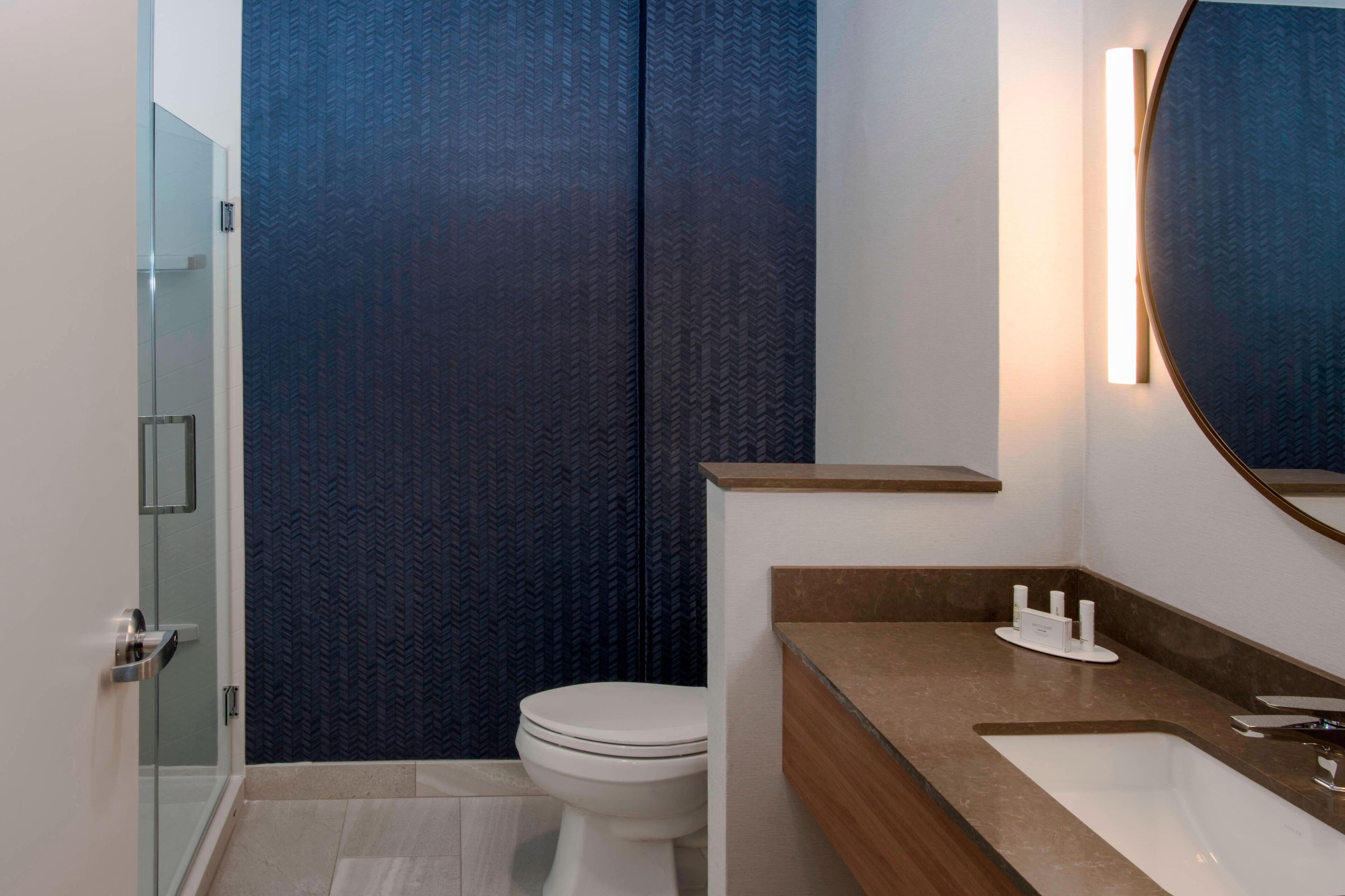 Un baño moderno con cabina de ducha de vidrio, inodoro blanco y tocador de madera con lavamanos.