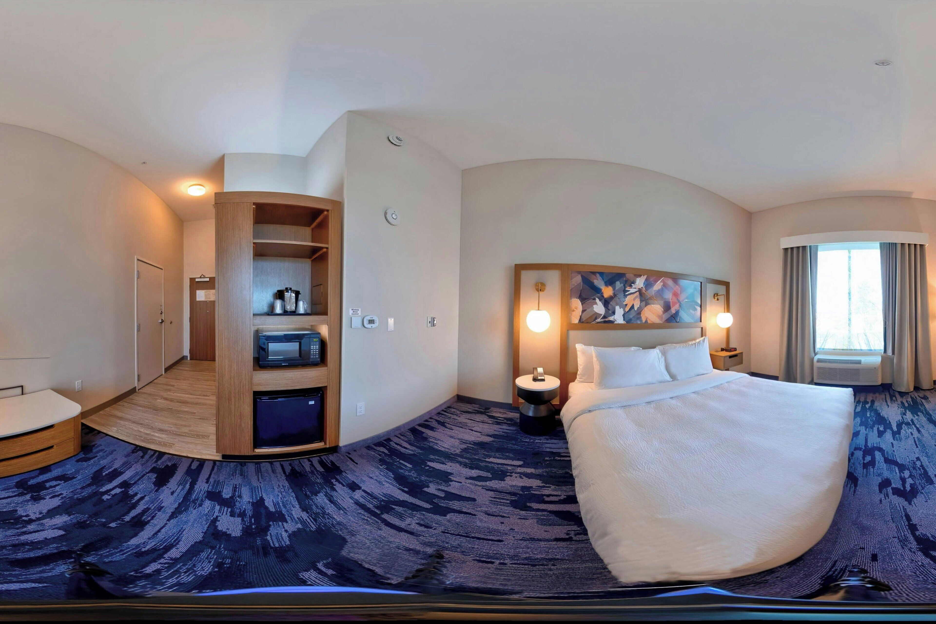 Een hotelkamer met een gebogen indeling, een bed, een bureau, een zithoek en een ingebouwde televisie.