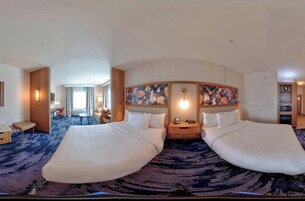 Habitación de hotel con dos camas, un ventanal grande, un escritorio y una silla.