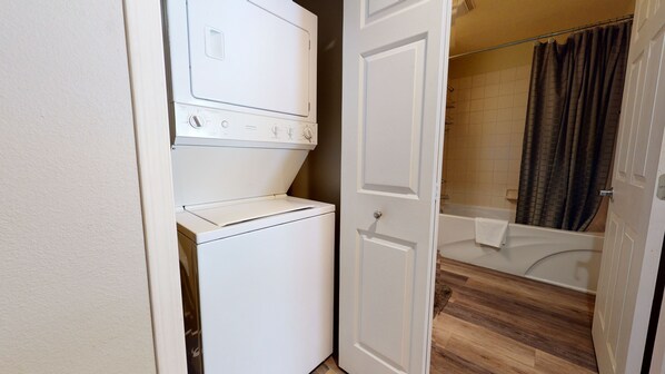 Une buanderie équipée d’une machine à laver et d’un sèche-linge superposés, avec un plancher en bois et une douche dotée d’un rideau.
