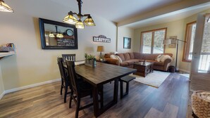 A dining area with a wooden table and chairs, a sofa, and a decorative wall with a clock and a sign saying "Life is Beautiful". - On Sierra Star Golf Course, Washer/Dryer, Quiet Location & On-site Pool (Mammoth Lakes)