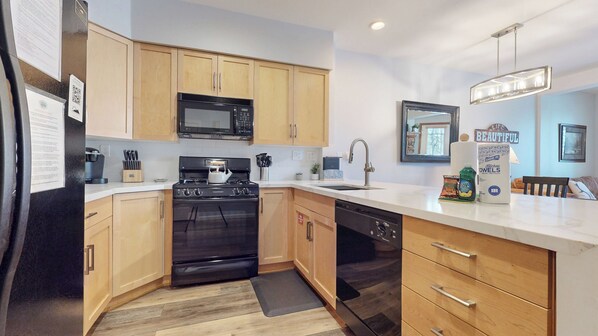 A modern kitchen with wooden cabinets, a black stove, a microwave, and a dishwasher.