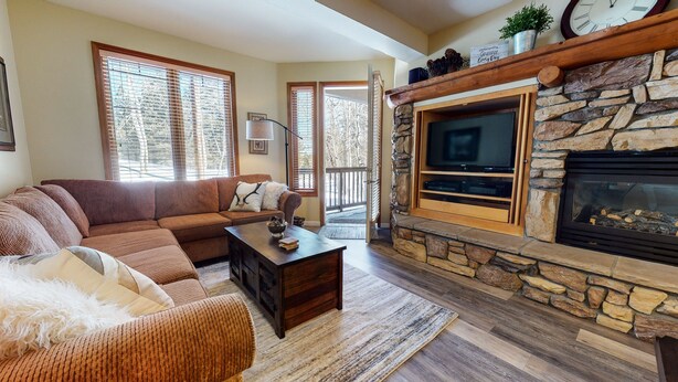 A cozy living room with a stone fireplace, a large flat-screen TV, and a comfortable sectional sofa. - On Sierra Star Golf Course, Washer/Dryer, Quiet Location & On-site Pool (Mammoth Lakes)
