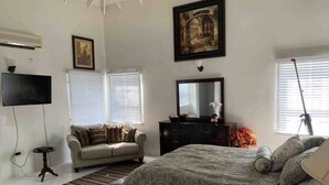 A bedroom with a bed, a sofa, a television, a dresser, and a painting on the wall.