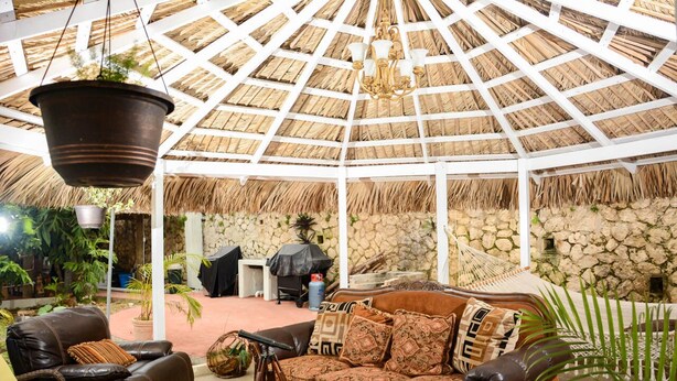 An outdoor seating area with a thatched roof, stone walls, and a hammock.