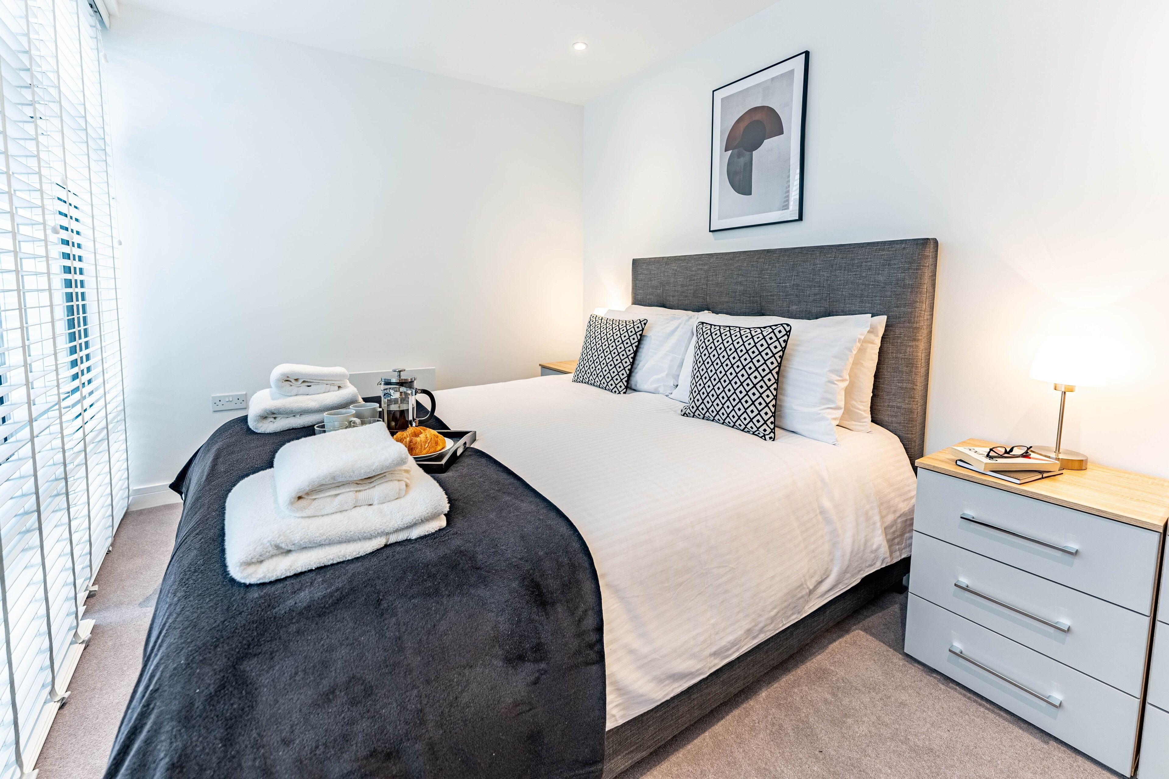 Een moderne hotelkamer met een groot bed, een nachtkastje met lamp en uitzicht op de stad.