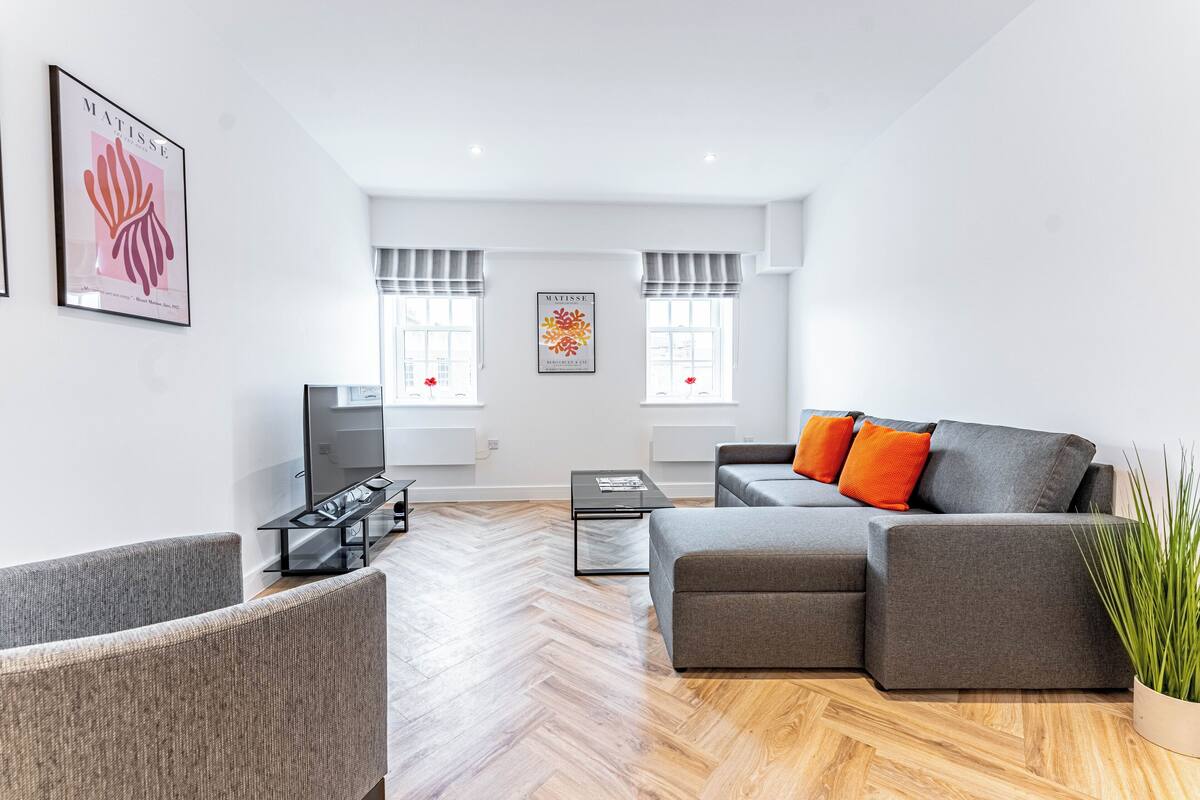 Una sala de estar moderna con un sofá gris, un televisor y dos cuadros enmarcados en la pared.